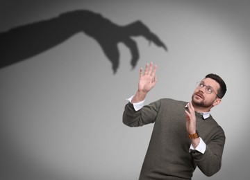 Image of Man scared by monstrous hand reaching for him. Creepy shadow on grey wall