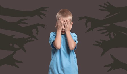 Teraphobia - fear of monsters. Scared boy covering his eyes on dark background. Silhouette of creepy hands behind child