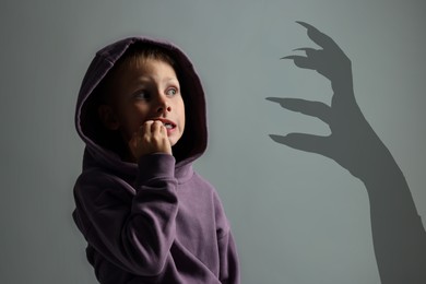 Image of Teraphobia - fear of monsters. Scared boy looking at creepy hand. Grey background