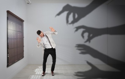 Image of Man scared by monstrous hands reaching for him. Creepy shadows in room