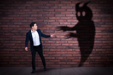 Businessman scared by monster. Scary shadow on brick wall