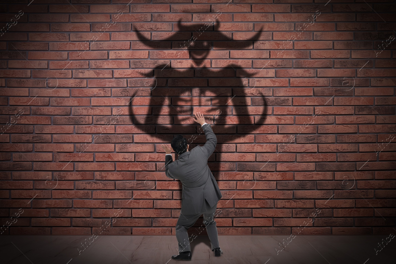 Image of Businessman scared by monster. Scary shadow on brick wall