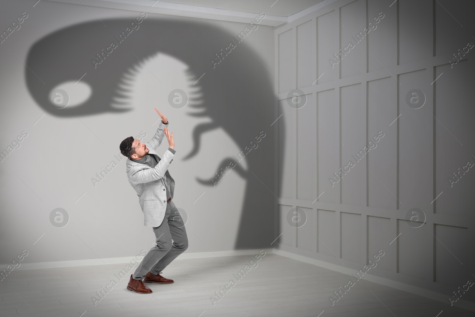 Image of Businessman scared by monster. Scary shadow in room