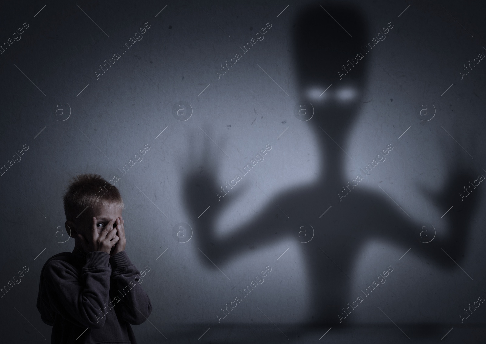 Image of Little kid scared by monster. Spooky shadow on grey wall