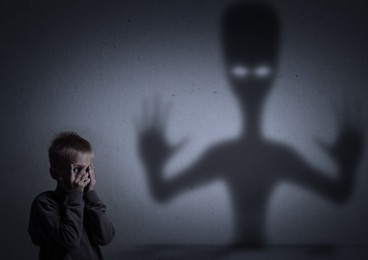 Little kid scared by monster. Spooky shadow on grey wall