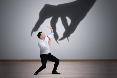 Image of Man scared by monstrous hand reaching for him. Creepy shadow on light wall