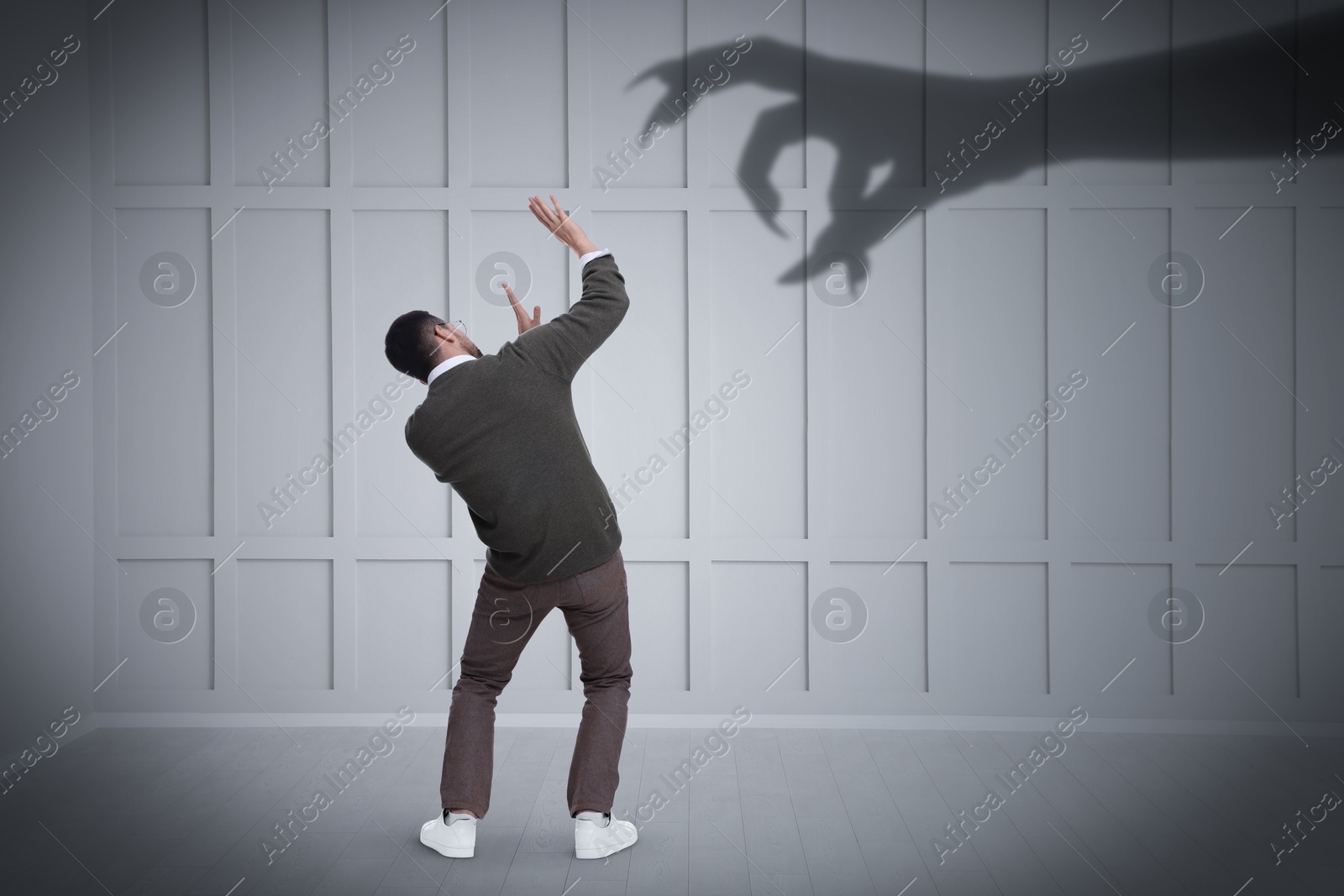 Image of Man scared by monstrous hand reaching for him. Creepy shadow on light wall