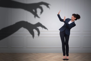 Image of Businesswoman scared by hands of monster reaching for her. Creepy shadow on white wall