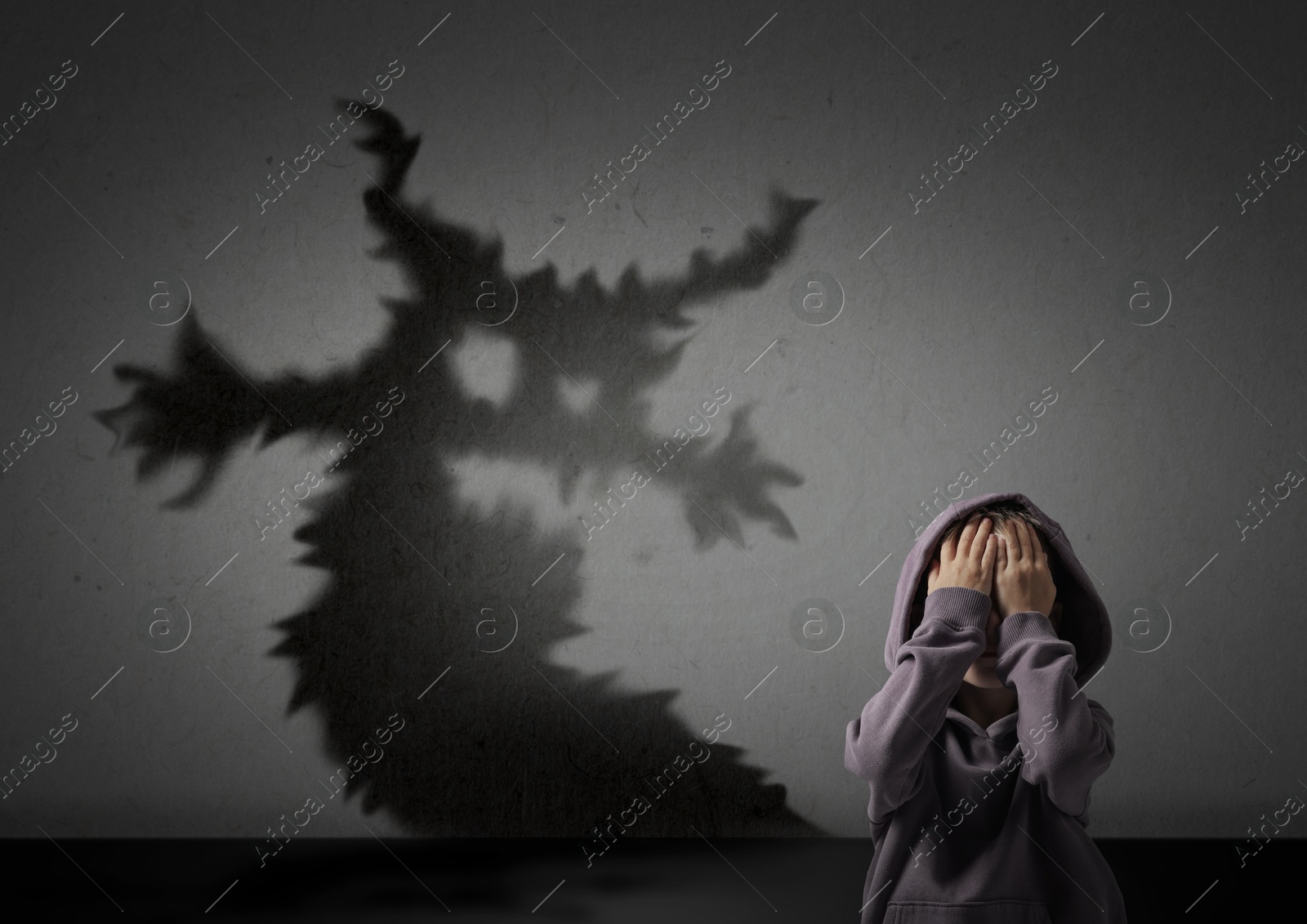 Image of Little kid scared by monster. Spooky shadow on grey wall