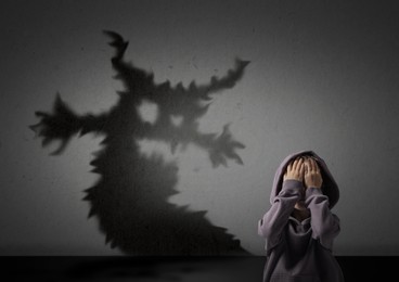 Image of Little kid scared by monster. Spooky shadow on grey wall