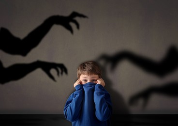 Image of Little child scared by monstrous hands reaching for him. Shadows on grey wall