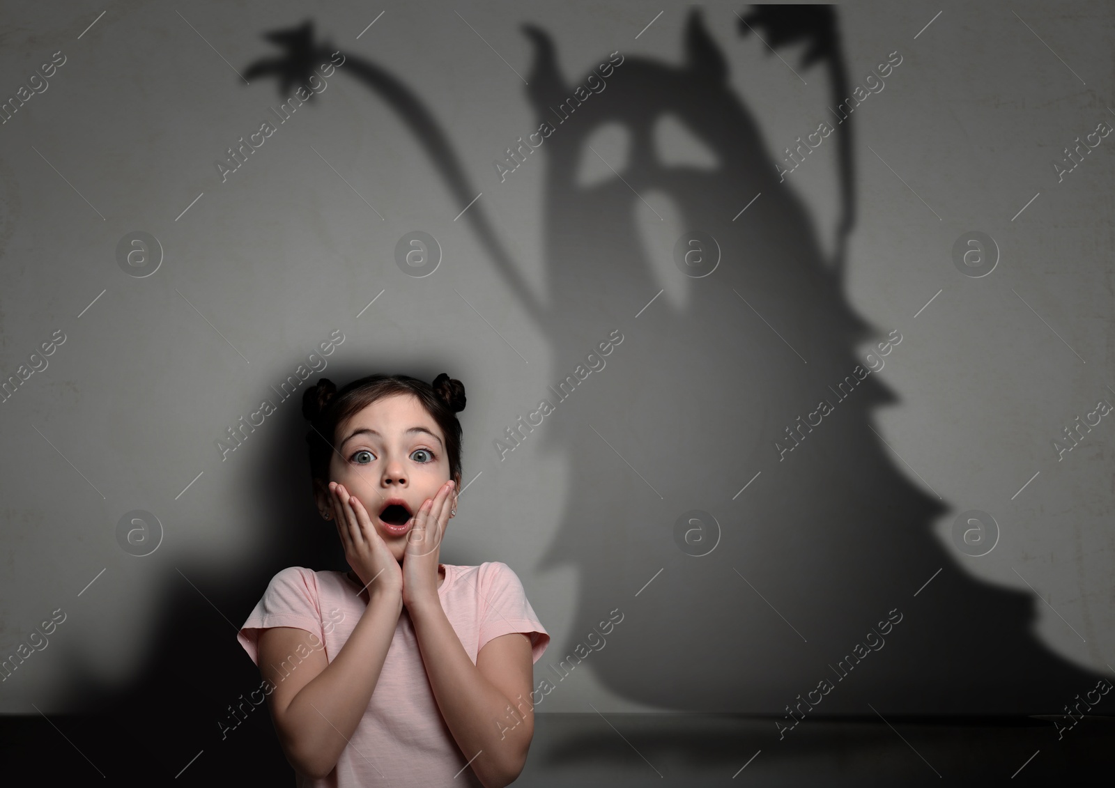 Image of Little kid scared by monster. Spooky shadow on grey wall