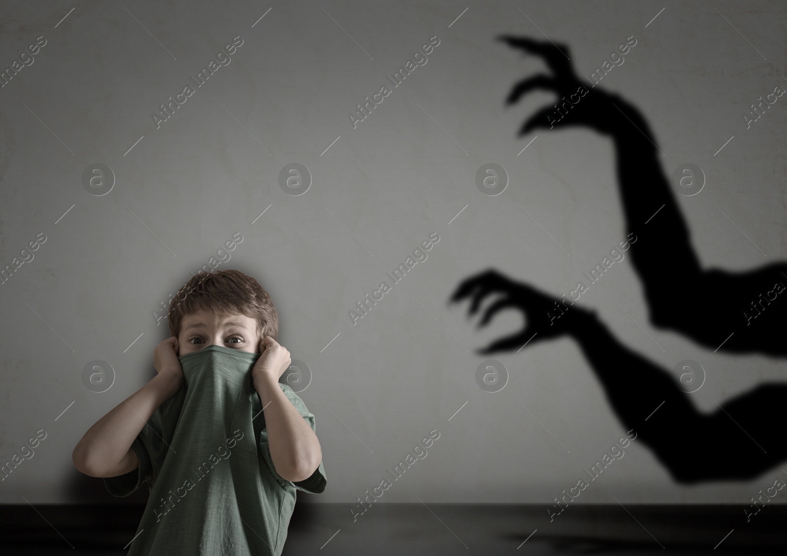 Image of Little kid scared by hands of monster reaching for him. Creepy shadow on grey wall