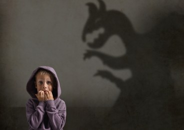 Image of Little kid scared by monster. Spooky shadow in wall