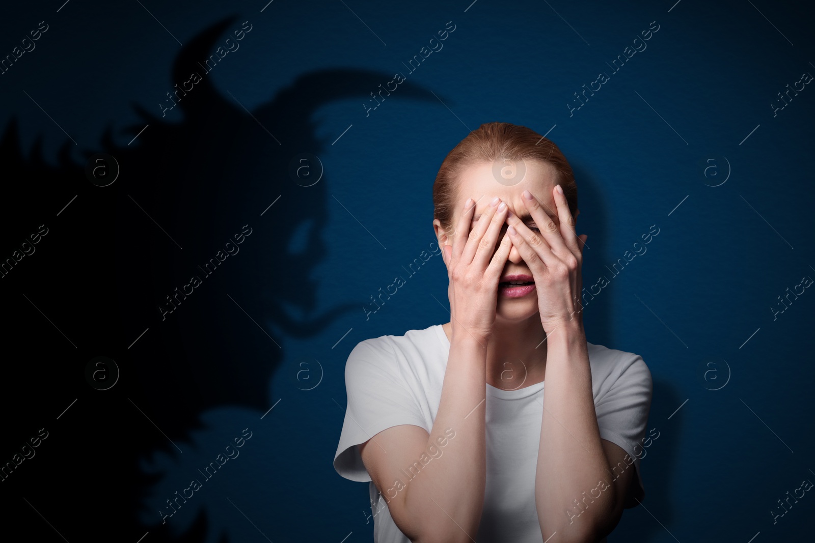 Image of Woman scared by monster. Creepy shadow on blue wall