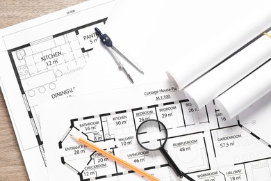 Photo of Different architectural drawings, dividers, pencil and magnifying glass on wooden table, top view