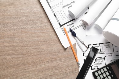 Photo of Different architectural drawings, ruler, pencil, calculator and dividers on wooden table, flat lay. Space for text