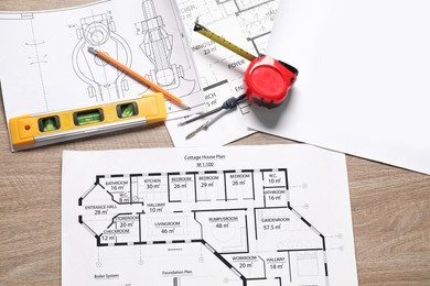 Photo of Different engineering drawings, building level, measuring tape, pencil and dividers on wooden table, flat lay