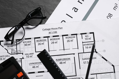 Different architectural drawings, glasses, calculator and ruler on grey textured table, flat lay