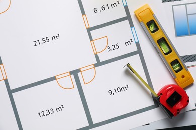 Building level and measuring tape on architectural drawings, flat lay