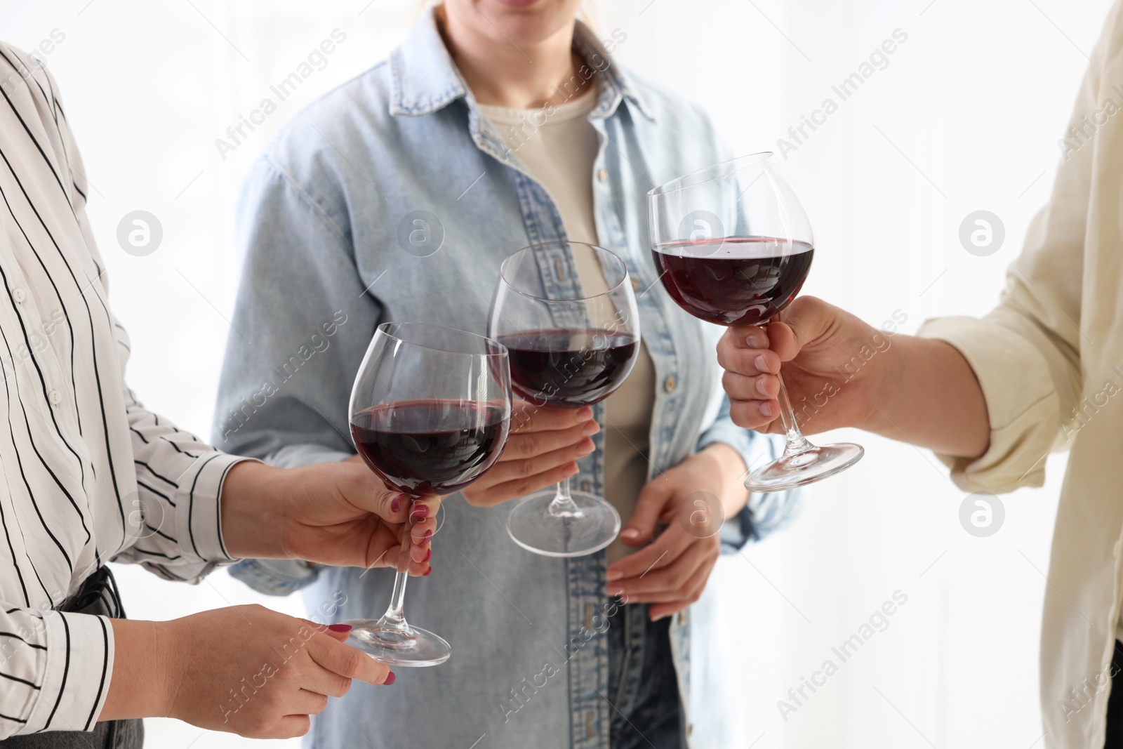 Photo of People clinking glasses of red wine indoors, closeup