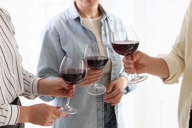 Photo of People clinking glasses of red wine indoors, closeup