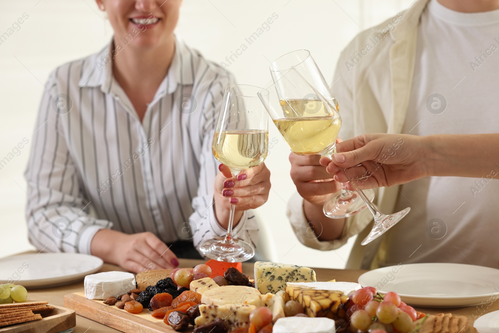 Photo of People clinking glasses of wine at served table, closeup