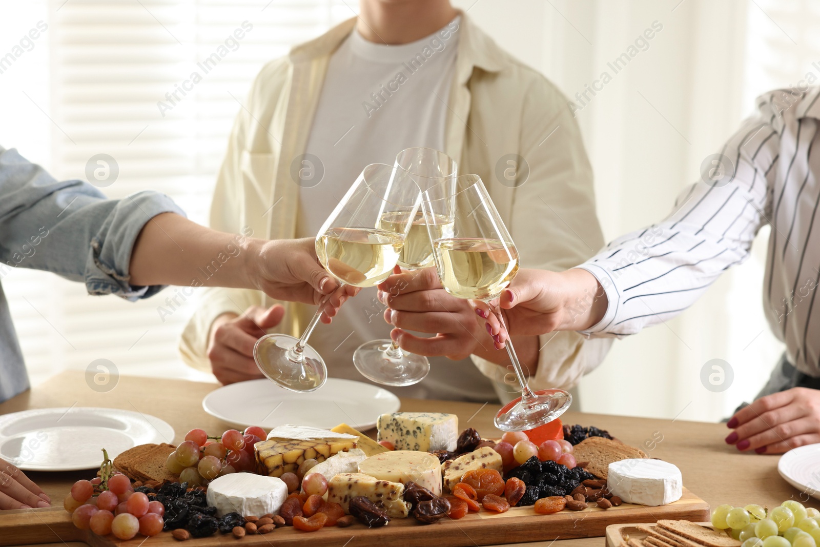 Photo of People clinking glasses of wine at served table, closeup