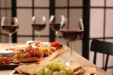 Photo of Glasses of red wine and different snacks on wooden table