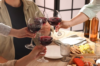 Photo of People clinking glasses of red wine at served table, closeup