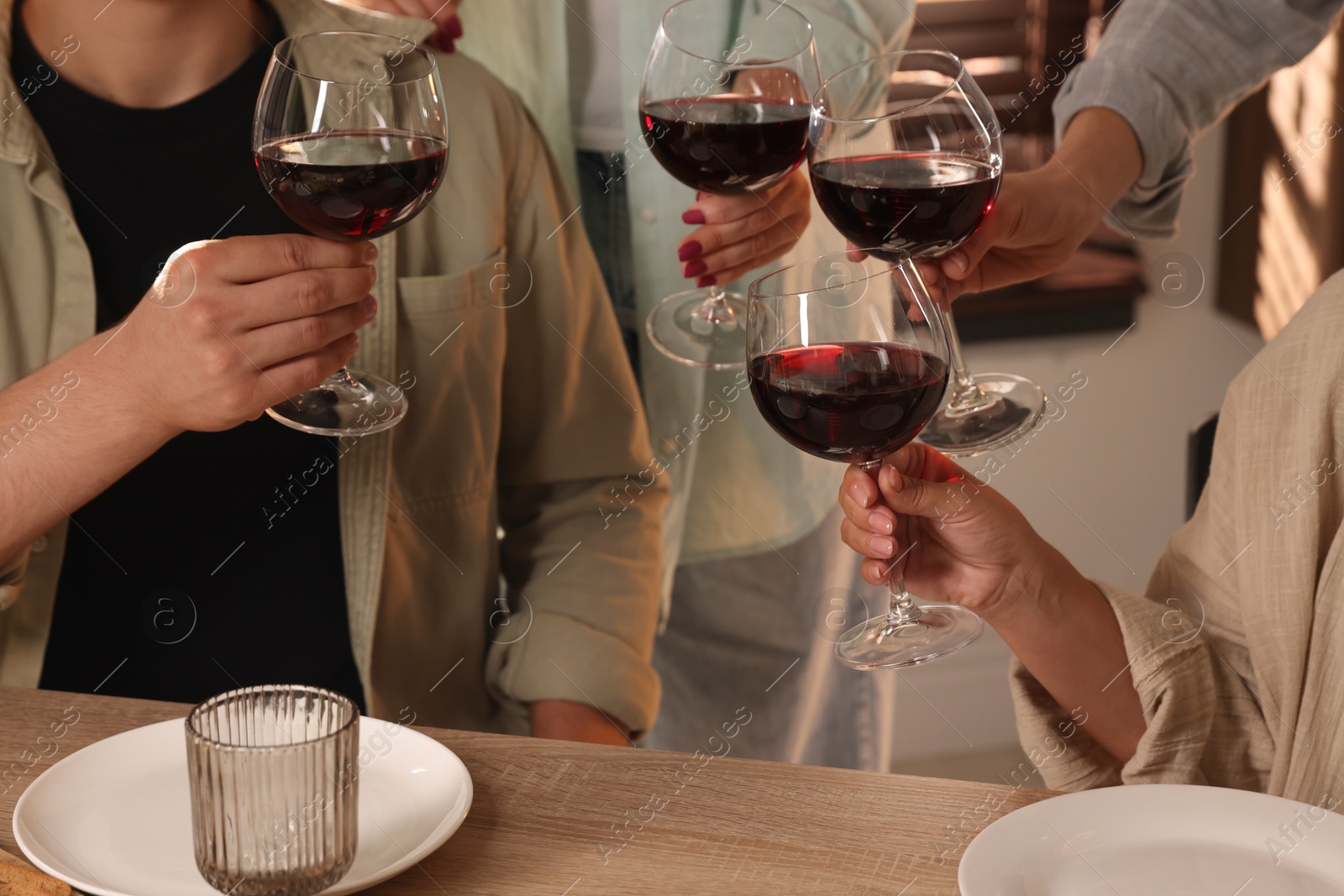 Photo of People clinking glasses of red wine at served table, closeup