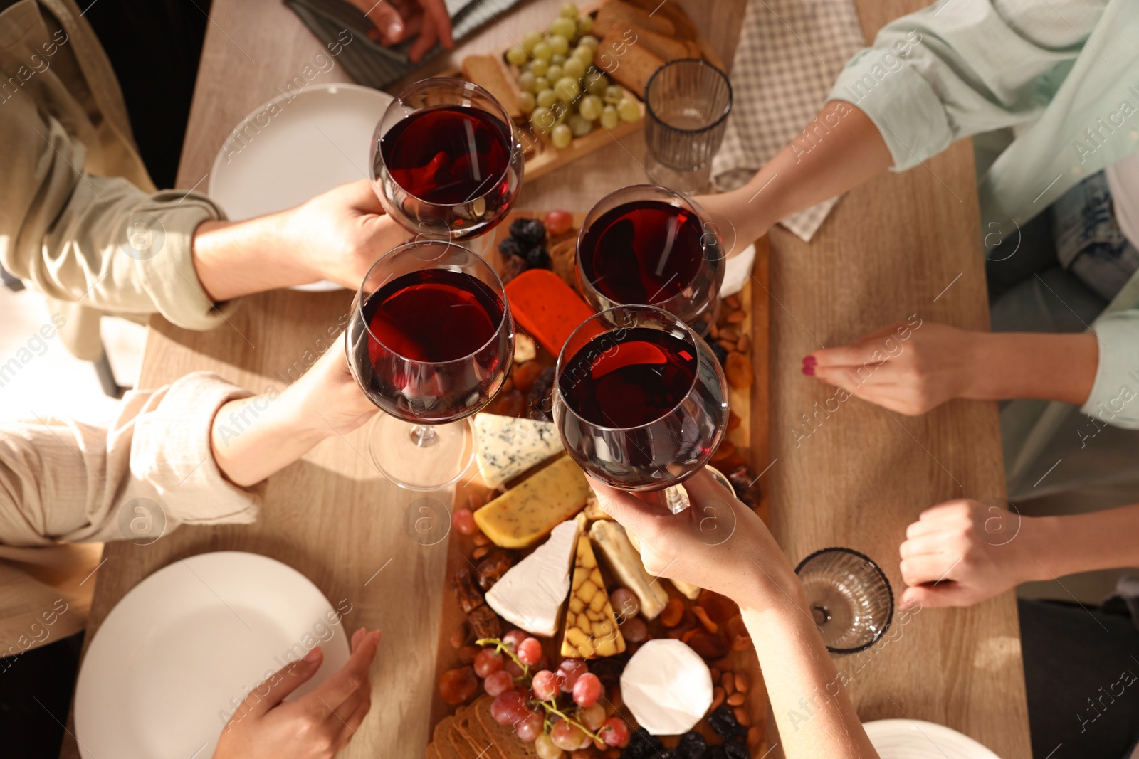 Photo of People clinking glasses of red wine at served table, top view