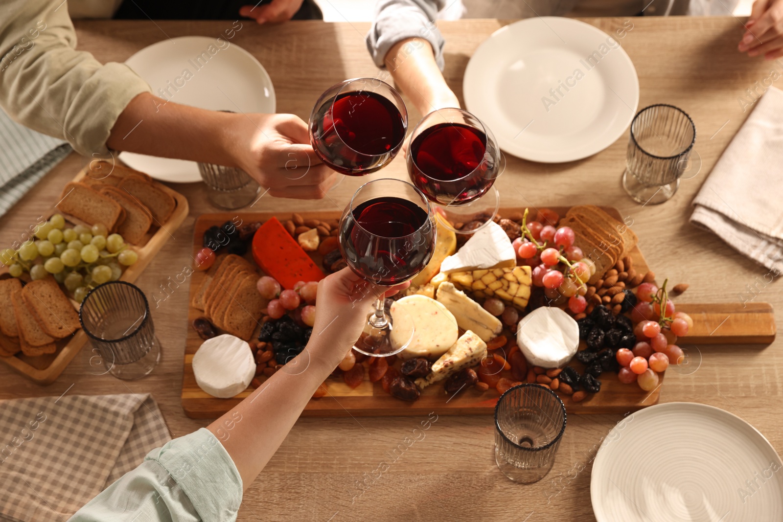 Photo of People clinking glasses of red wine at served table, closeup