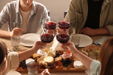 Photo of People clinking glasses of red wine at served table, closeup