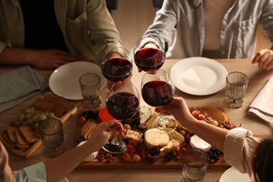 Photo of People clinking glasses of red wine at served table, closeup