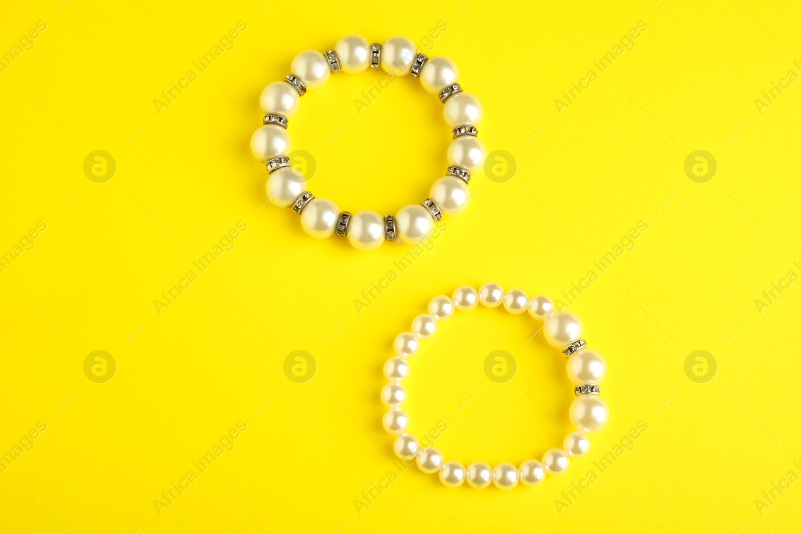 Photo of Beautiful bijouterie. Stylish bracelets on yellow background, top view