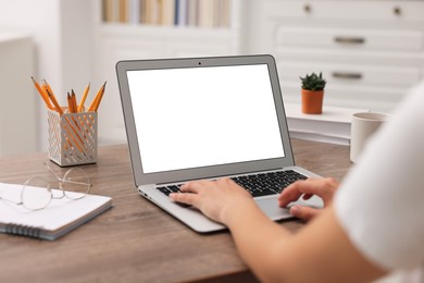 Photo of Woman working with laptop at wooden table in office, closeup. Mockup for design