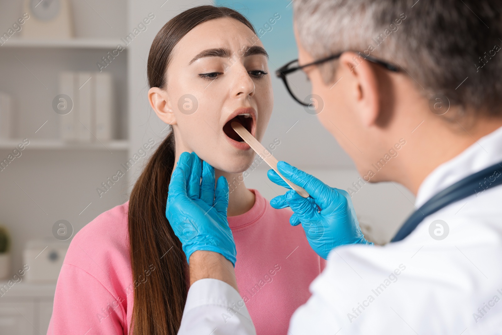 Photo of Doctor examining woman's throat with tongue depressor in clinic