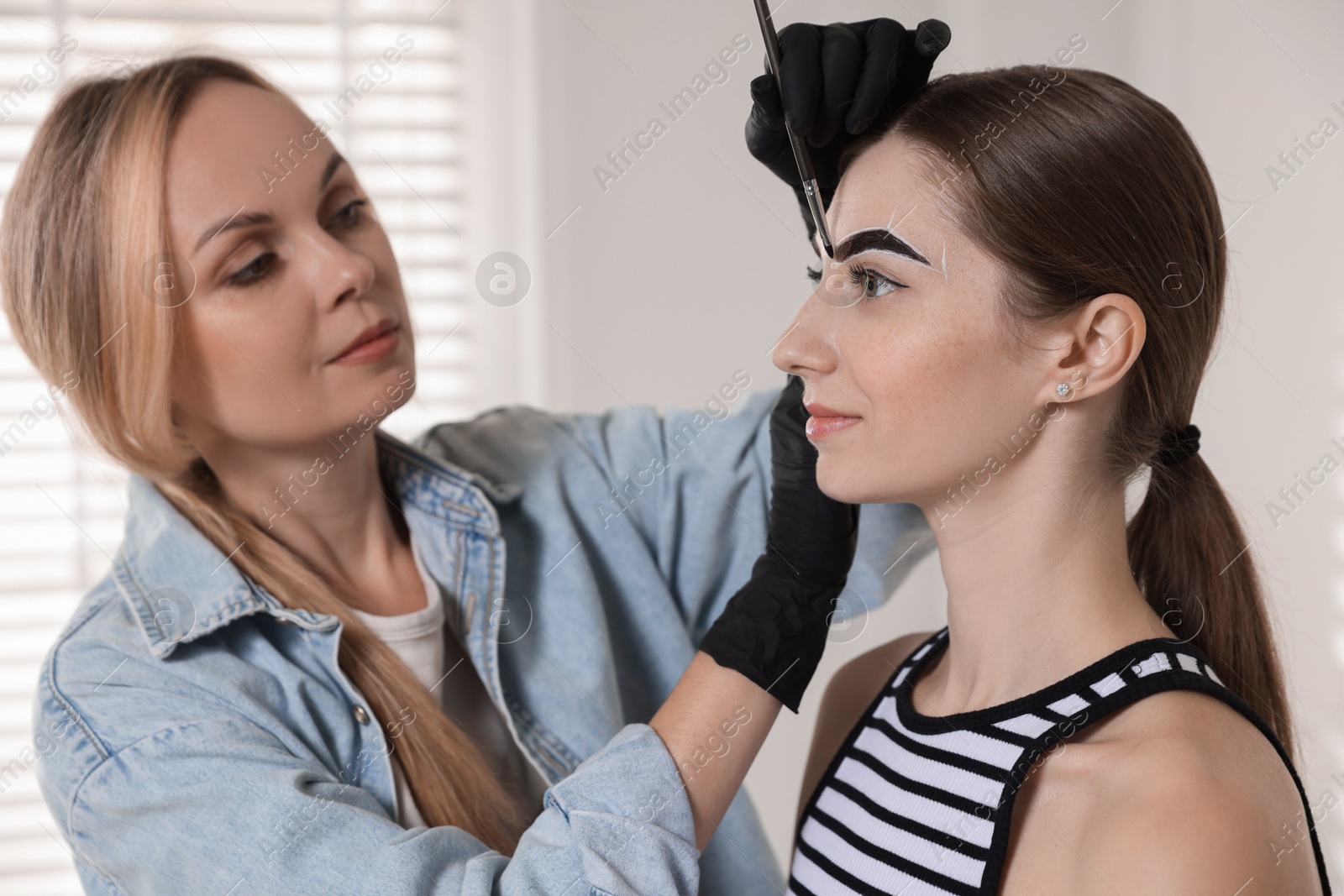 Photo of Beautician dyeing client’s eyebrows with henna in salon, selective focus