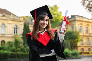 Photo of Happy student with diploma after graduation ceremony outdoors