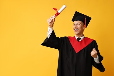 Photo of Happy student with diploma after graduation on orange background. Space for text