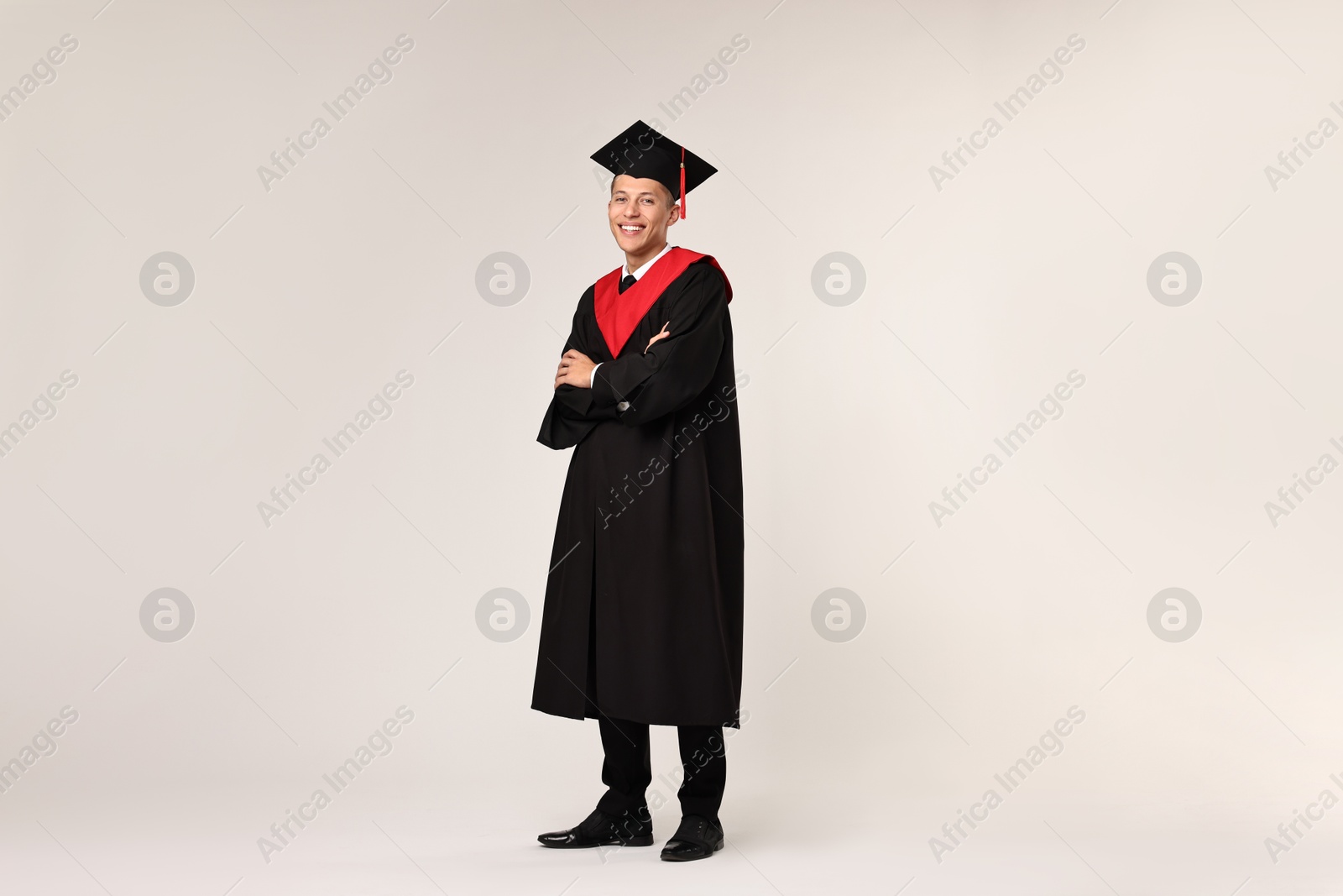 Photo of Happy student with crossed arms after graduation on light grey background