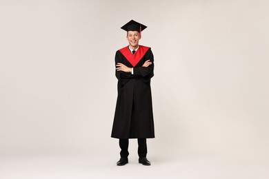 Happy student with crossed arms after graduation on light grey background