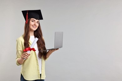 Photo of Happy student with laptop and diploma after graduation on grey background. Space for text