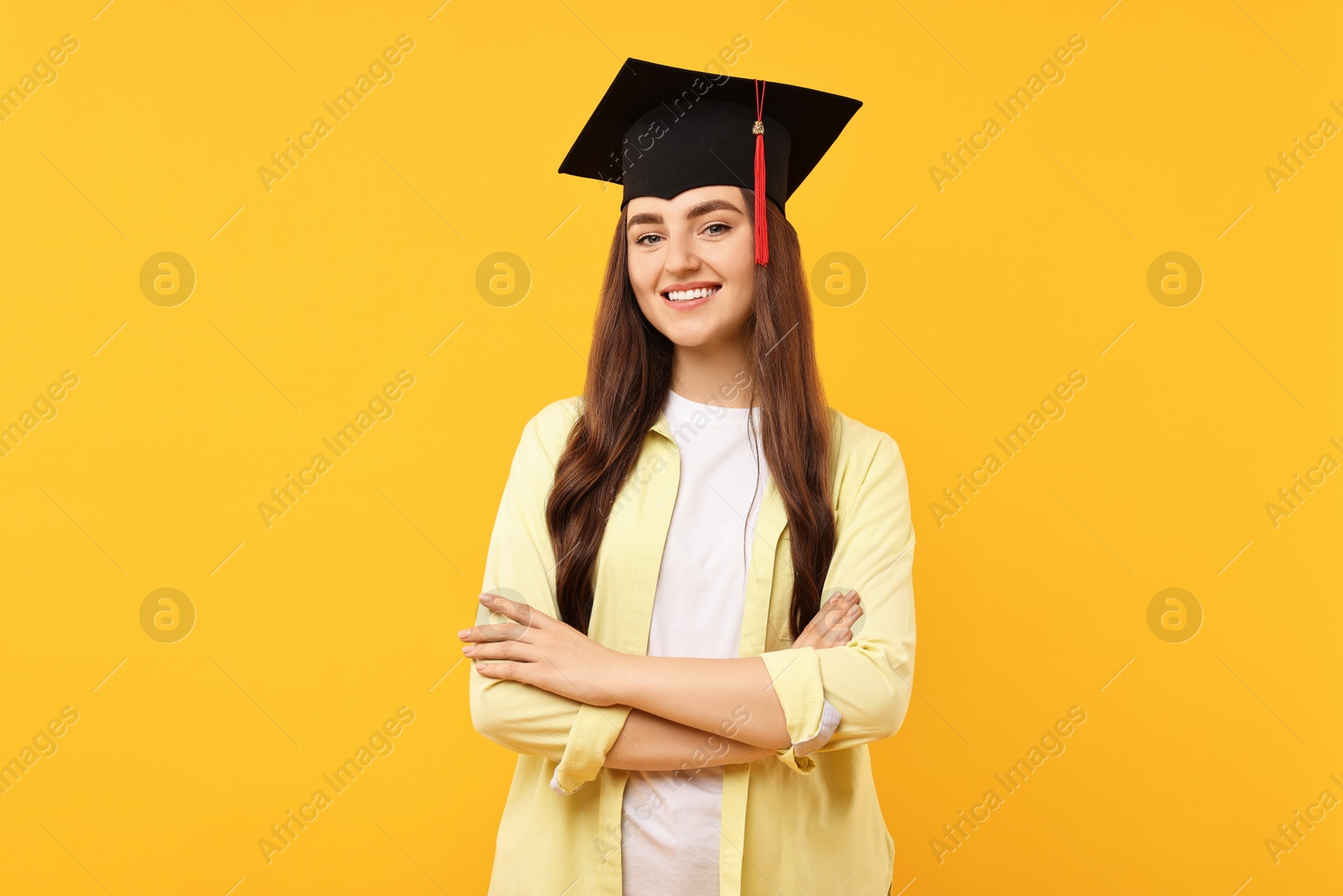 Photo of Happy student with crossed arms after graduation on orange background