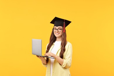 Photo of Happy student with laptop after graduation on orange background