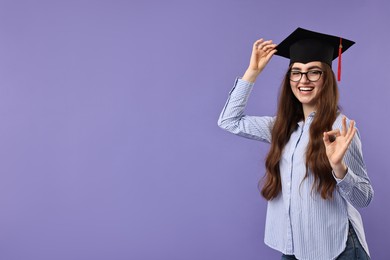 Photo of Happy student showing ok gesture after graduation on violet background. Space for text