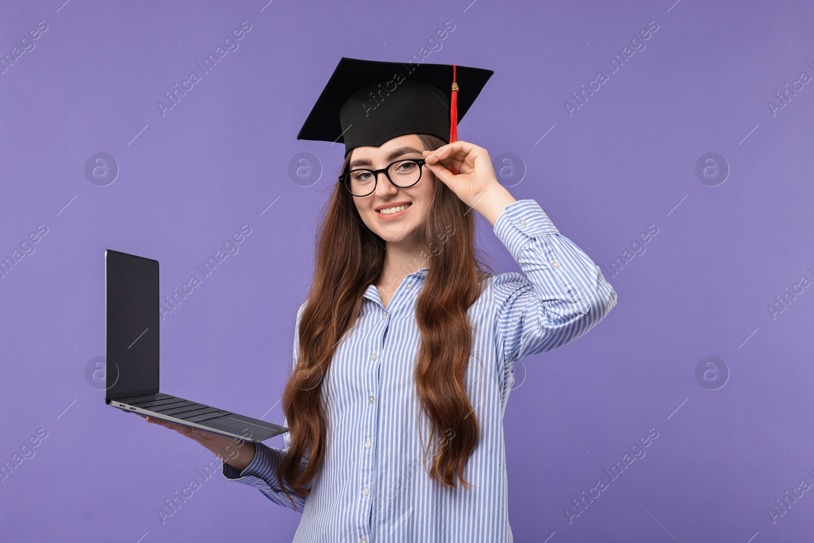 Photo of Happy student with laptop after graduation on violet background