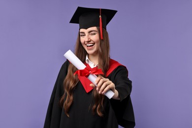 Photo of Happy student with diploma after graduation on violet background