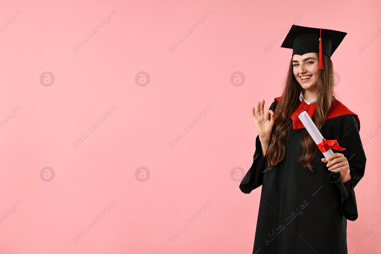 Photo of Happy student with diploma after graduation showing ok gesture on pink background. Space for text